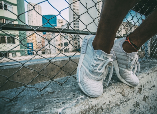 White Adidas sneakers against a wire fence